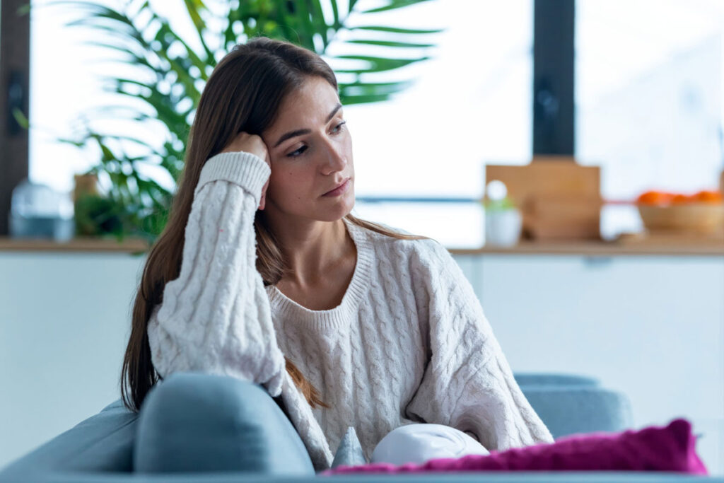 Shot of depressed young woman thinking about her problems while sitting on the sofa at home.