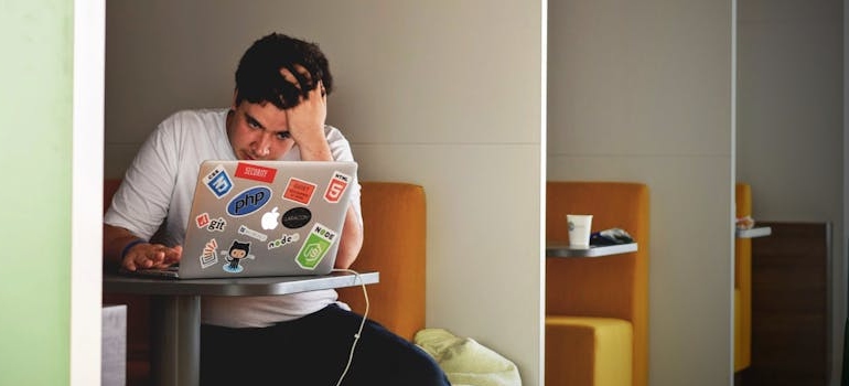 a man holding his head while reading about daily routines to overcome gambling urges and manage anxiety on his laptop